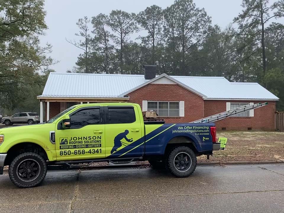 Johnson Roofing Solutions Roofing, Siding, Gutters company truck outside a home in Lynn Haven Florida while roofers install a new metal roof | Commercial and residential roofing company serving the Florida Panhandle with roofing, siding, & gutter installations, repairs & more