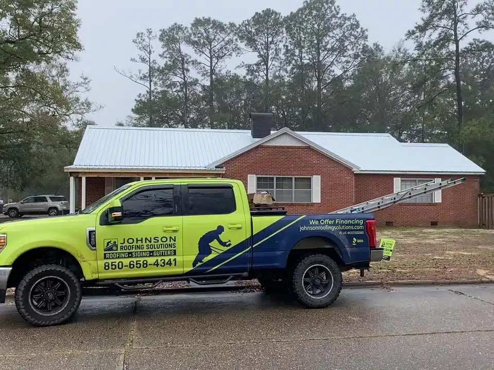Johnson Roofing Solutions Roofing, Siding, Gutters company truck outside a home in Lynn Haven Florida while roofers install a new metal roof | Commercial and residential roofing company serving the Florida Panhandle with roofing, siding, & gutter installations, repairs & more